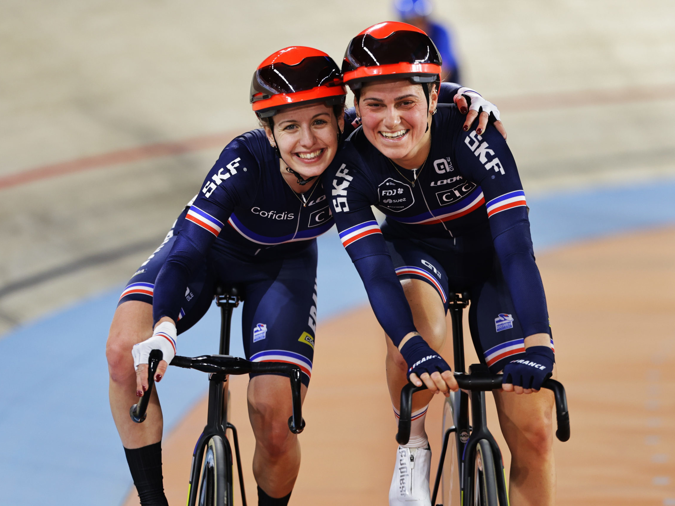 Two female cyclists with their arms round each other's shoulders smiling at the camera