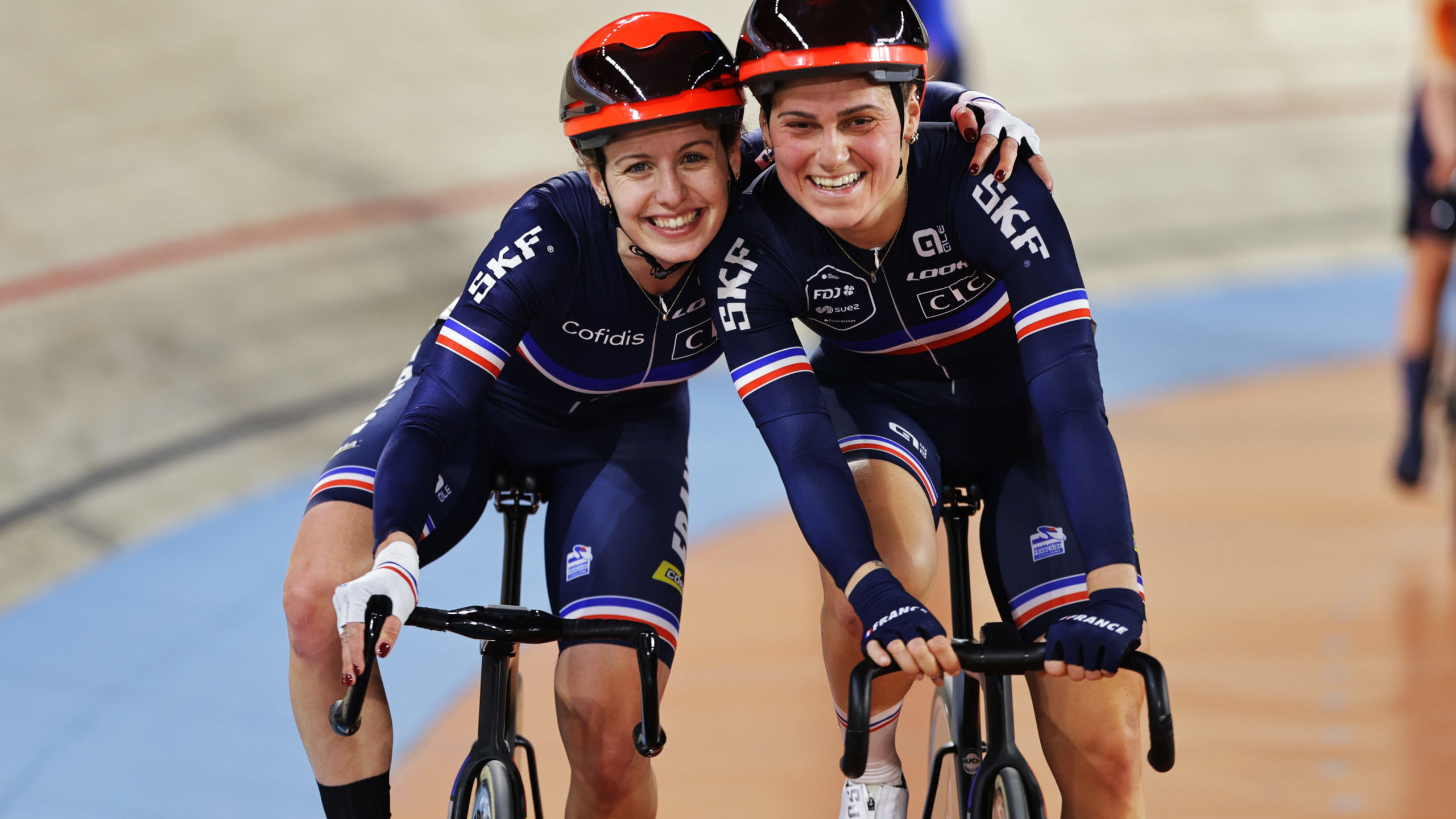 Two female cyclists with their arms round each other's shoulders smiling at the camera