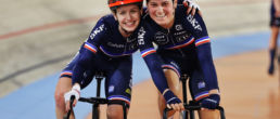 Two female cyclists with their arms round each other's shoulders smiling at the camera