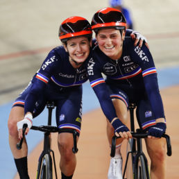 Two female cyclists with their arms round each other's shoulders smiling at the camera