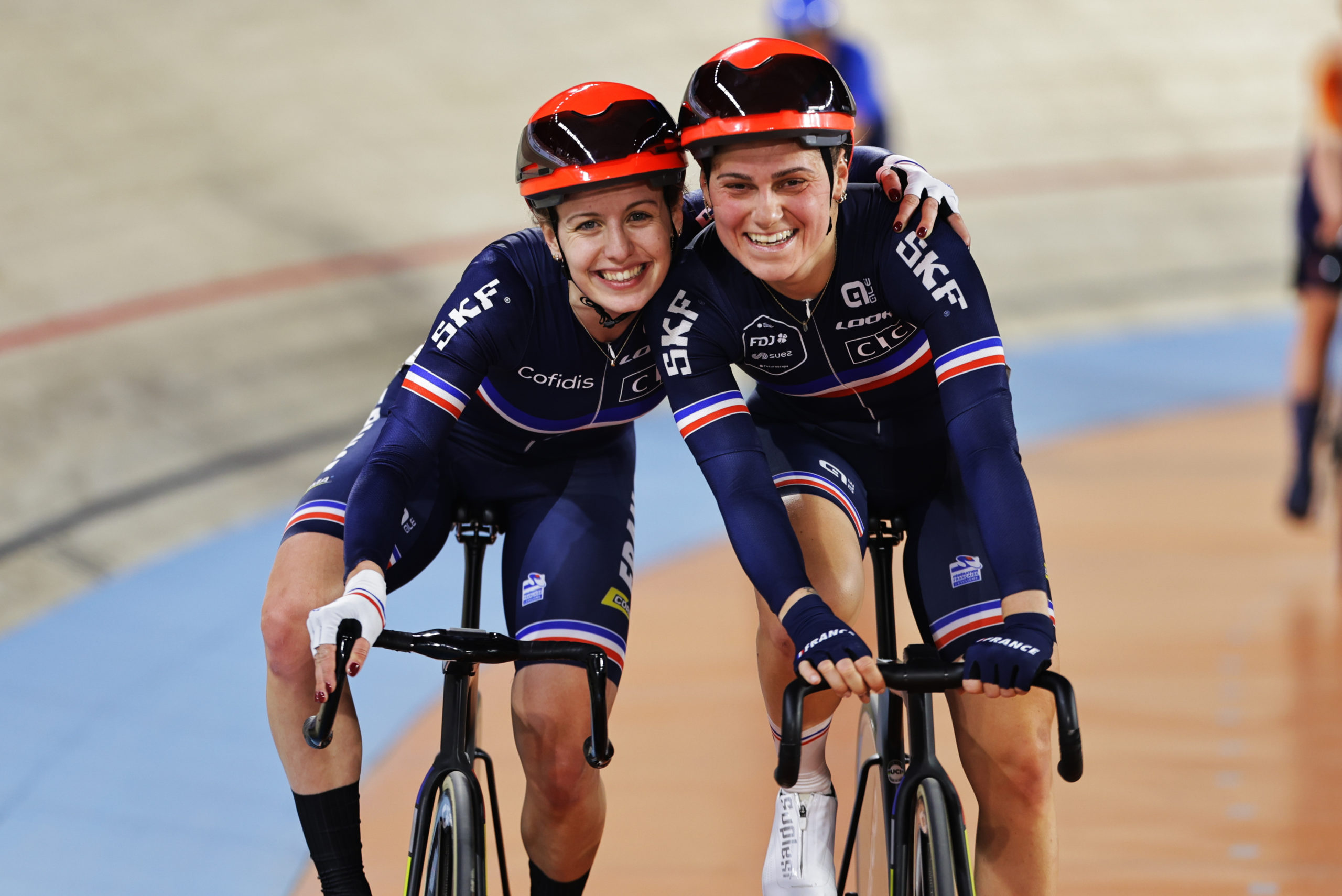 Two female cyclists with their arms round each other's shoulders smiling at the camera