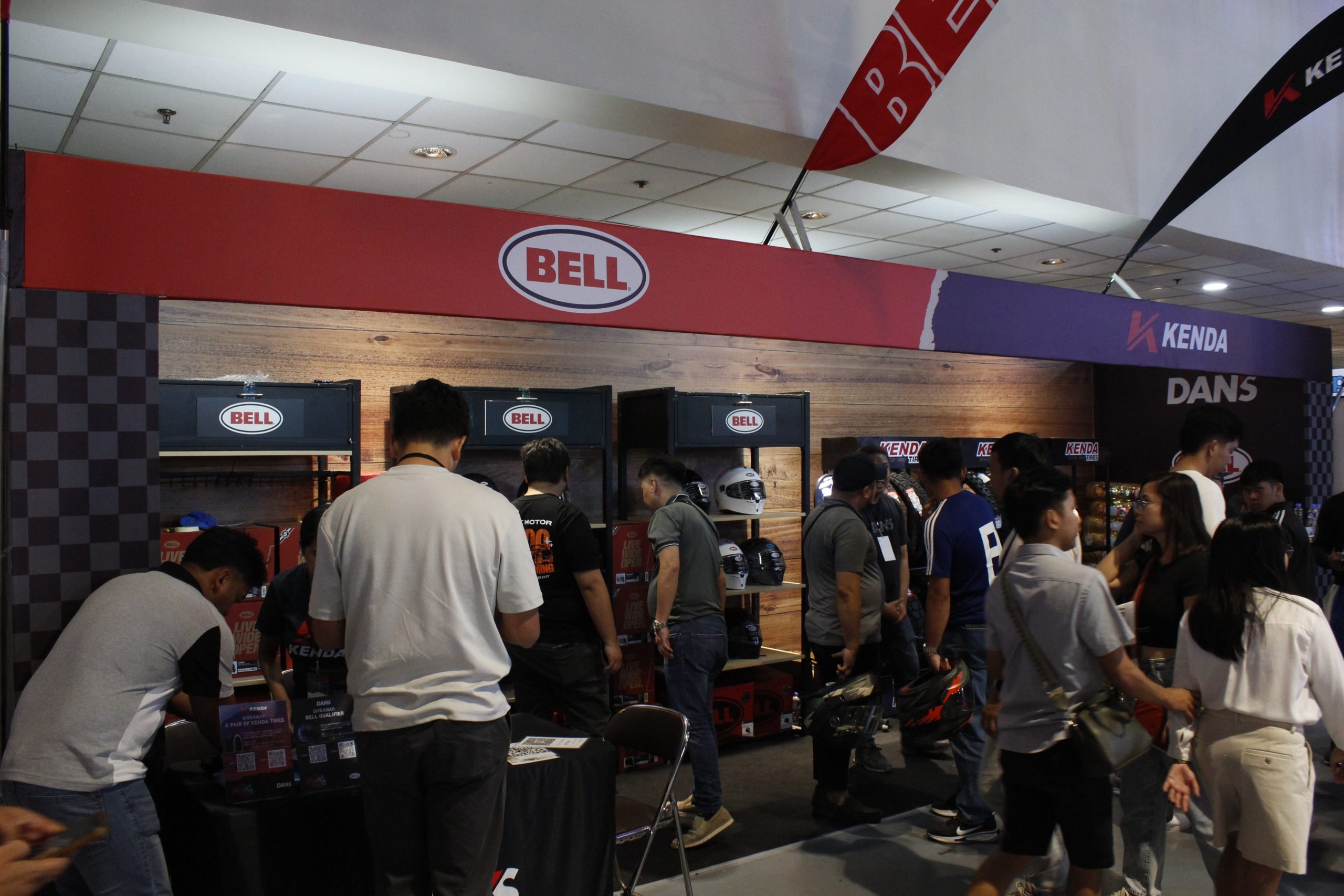 Bell helmets stand at a exhibition with people standing around it